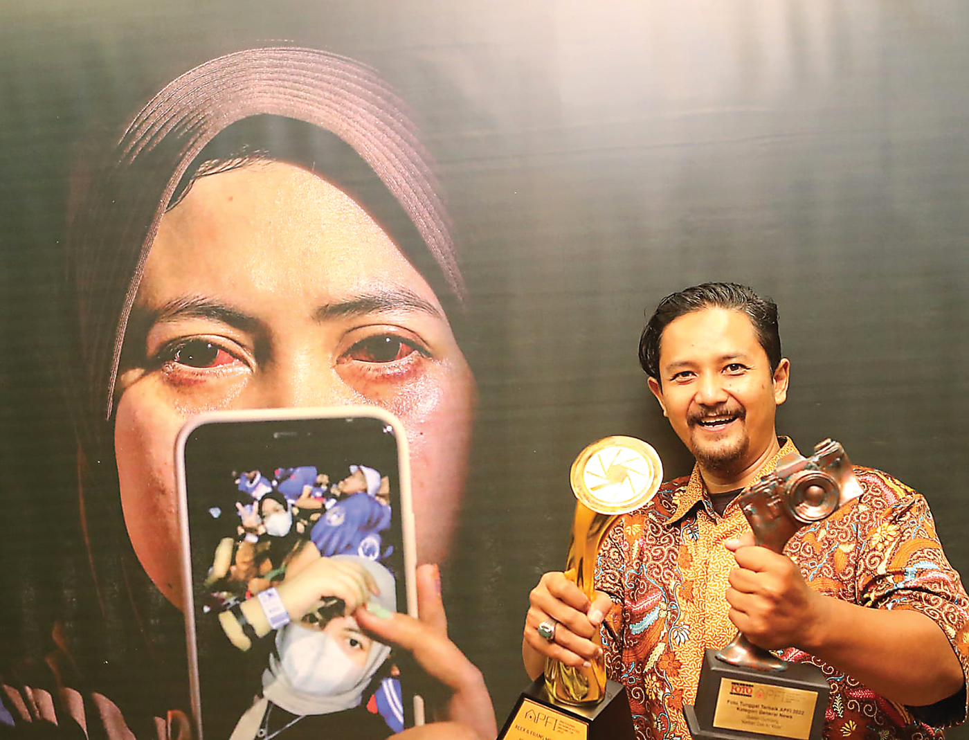 SABET PENGHARGAAN: Guslan Gumilang dan dua piala yang diraihnya di depan karya fotonya di pameran APFI di Balai Budaya, Surabaya, kemarin. - Image