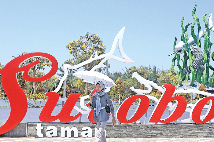 TERIK: Seorang warga berjalan dengan memakai payung di Taman Suroboyo, Senin (25/9). Peningkatan suhu di Surabaya memicu kasus ISPA. - Image