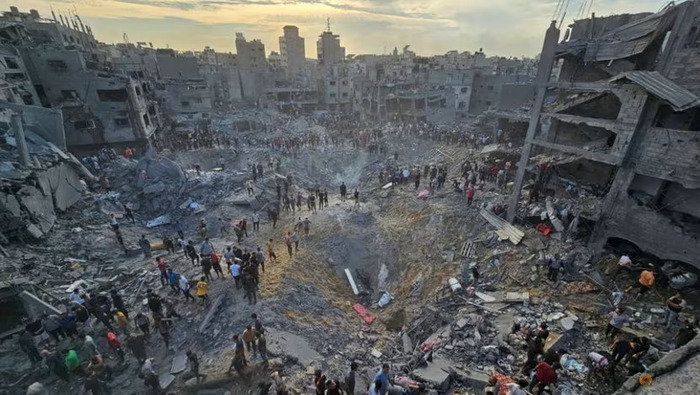 Ledakan bom membuat lubang besar bak kawah di tengah bangunan beton yang hancur di sekelilingnya, warga Palestina mencari korban di lokasi kamp pengungsi Jabalia, Gaza pada Rabu (31/10)./ - Image
