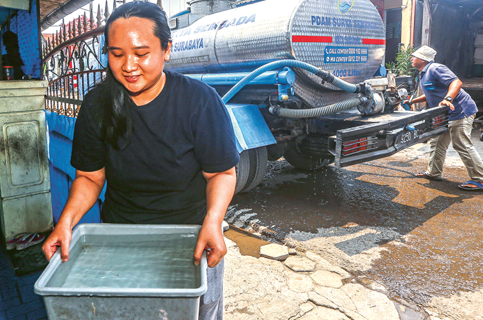 TAMPUNG AIR: Warga RT 06, RW 05, Manukan Rejo, Desi mengambil air dari mobil tangki PDAM, lalu memasukkannya ke bak air di rumahnya kemarin (8/11). Di beberapa RW Manukan Rejo, air PDAM belum mengalir - Image