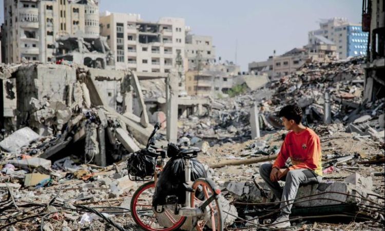 Seorang pemuda Palestina duduk di samping sepedanya di tengah puing-puing bangunan yang hancur di Kota Gaza di jalur Gaza utara setelah berminggu-minggu pemboman Israel. - Image