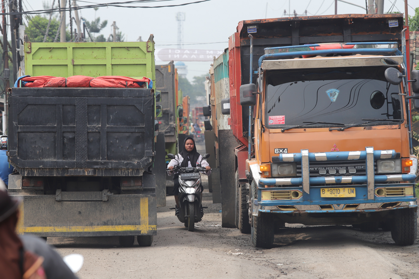 Pegendara sepeda motor melewati jalan yang terhimpit di antara dua badan truk yang antre melintas di Jalan Raya Parung Panjang, Bogor, Jawa Barat, Sabtu (9/12/2023). Kemacetan imbas dari sejumlah sopir truk berunjuk rasa terkait jam operasional truk tamb - Image