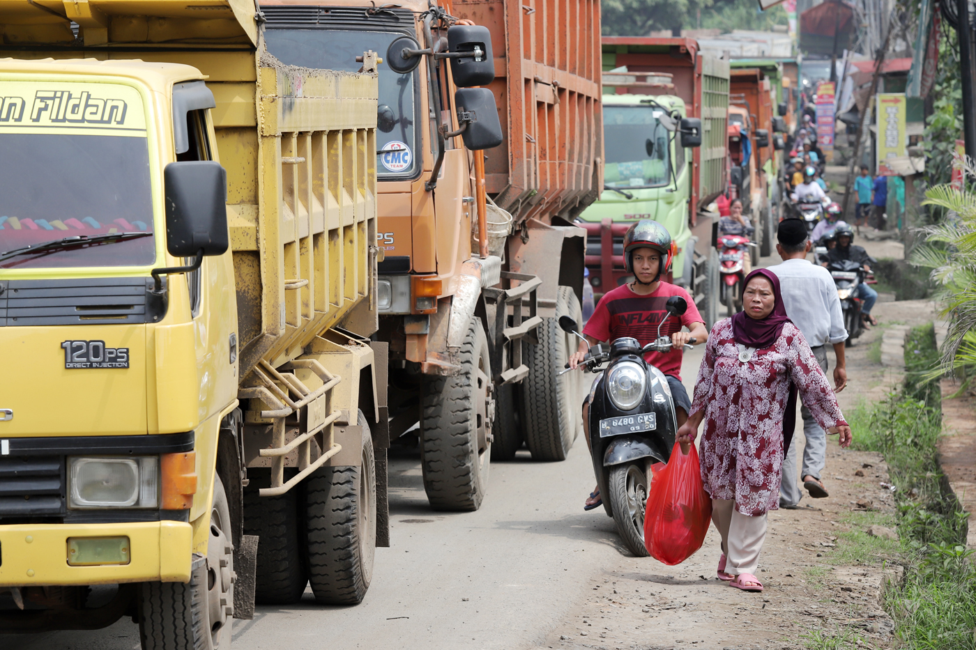 ILUSTRASI: Pejalan kaki dan pesepeda motor melintas di antara truk yang antre melintas di Jalan Raya Parung Panjang, Bogor, Jawa Barat, Sabtu (9/12/2023). (DERY RIDWANSAH/ JAWAPOS.COM) - Image