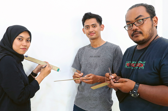 LESTARIKAN BUDAYA: Dari kiri, Rifa’tul Hasanah, Andri Setyo Nugroho, dan Aditya Sukma Caesara saat menulis aksara Jawa kuno di daun lontar. - Image