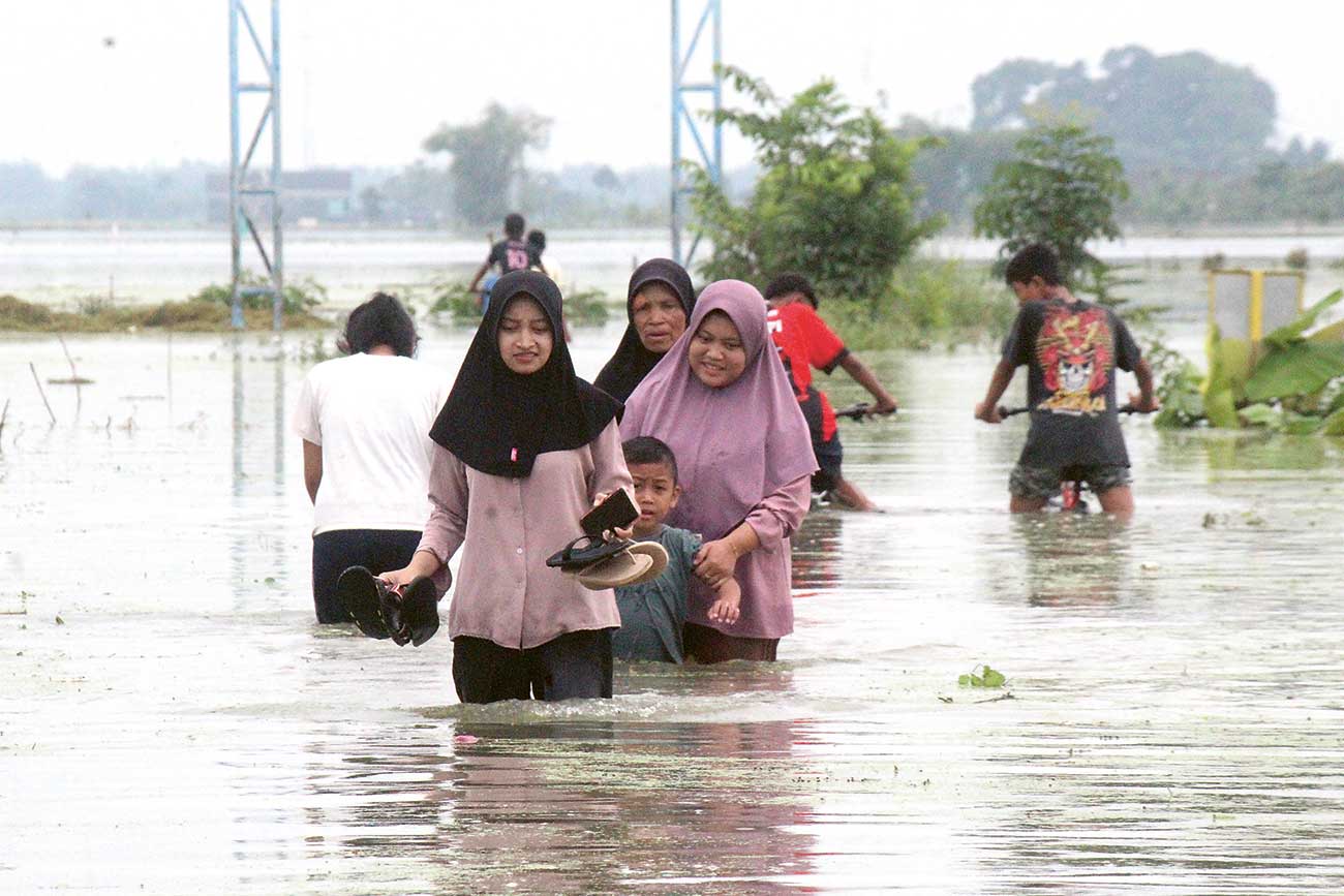 TERGENANG: Masyarakat melewati jalan di Dunun Mejeruk, Desa Bulurejo, Kecamatan Rengel, Kabupaten Tuban, Jawa Timur, pasca luapan Sungai Bengawan Solo, Selasa (12/3). - Image