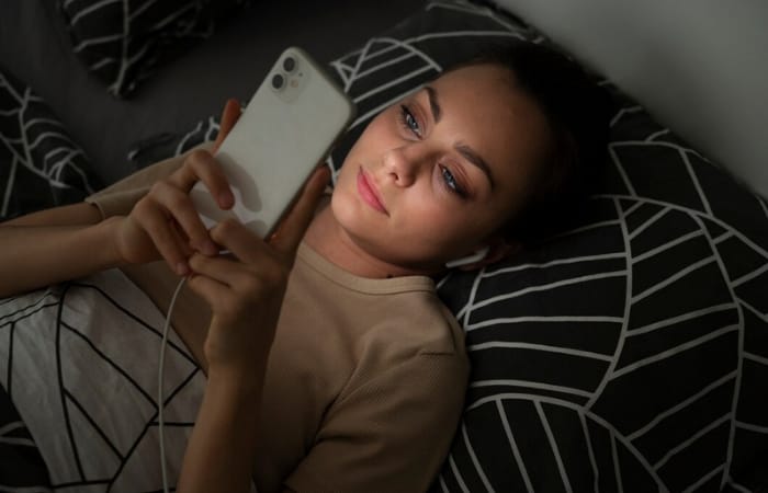Ilustrasi wanita yang sedang memakai gadget sebelum tidur yang membuat begadang hingga dini hari sehingga menyebabkan pola tidur berantakan (freepik) - Image