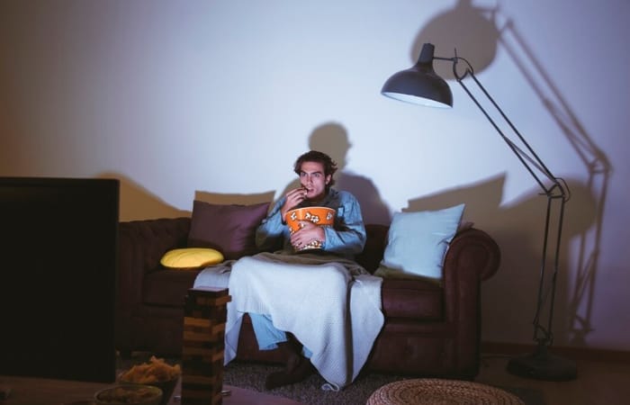 Ilustrasi pria yang menonton film di malam hari sebagai salah satu kebiasaan orang yang tidak sukses dan tidak maju dalam hidup (freepik) - Image