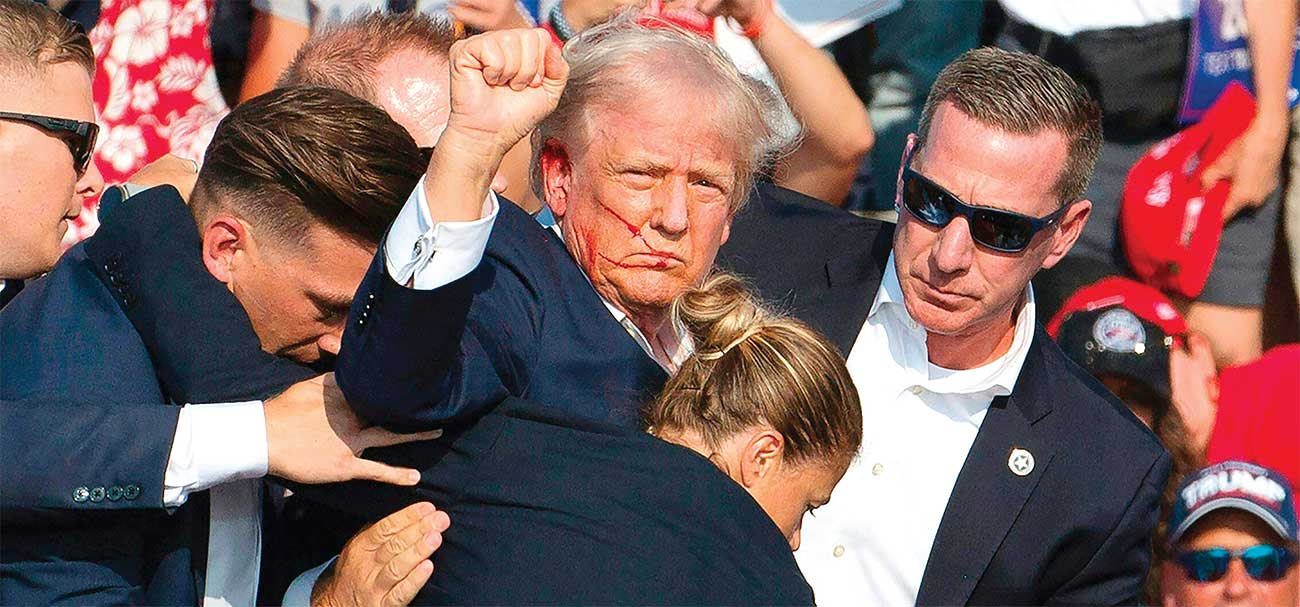 DARAH DI WAJAH KANDIDAT: Donald Trump dikelilingi petugas Secret Service dan dibawa turun dari panggung kampanye di Butler, Pennsylvania (13/7). (REBECCA DROKE/AFP) - Image