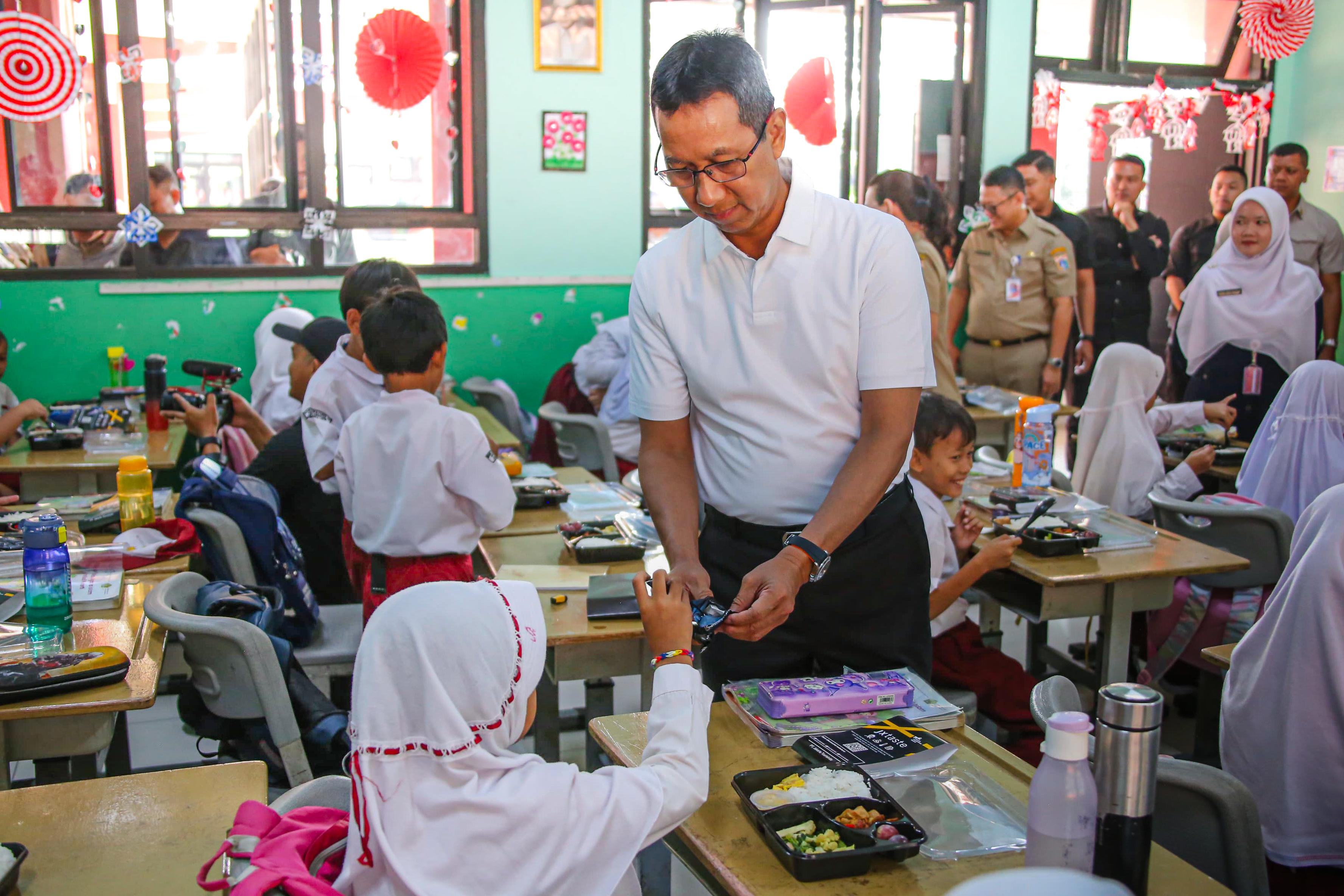 Penjabat Gubernur DKI Jakarta Heru Budi Hartono berbincang dengan siswa SDN 04 Pagi Cipayung, Jakarta Timur saat uji coba makan bergizi gratis, Senin (26/8). (dok. Humas Pemprov DKI Jakarta) - Image