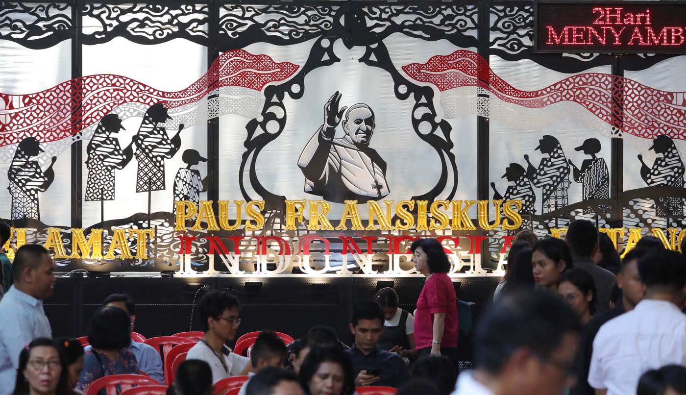 Warga berjalan di depan dekorasi bergambar Paus Fransiskus yang terpasang di Gereja Katedral Jakarta, Minggu (1/9/2024). (Fedrik Tarigan/ Jawa Pos) - Image