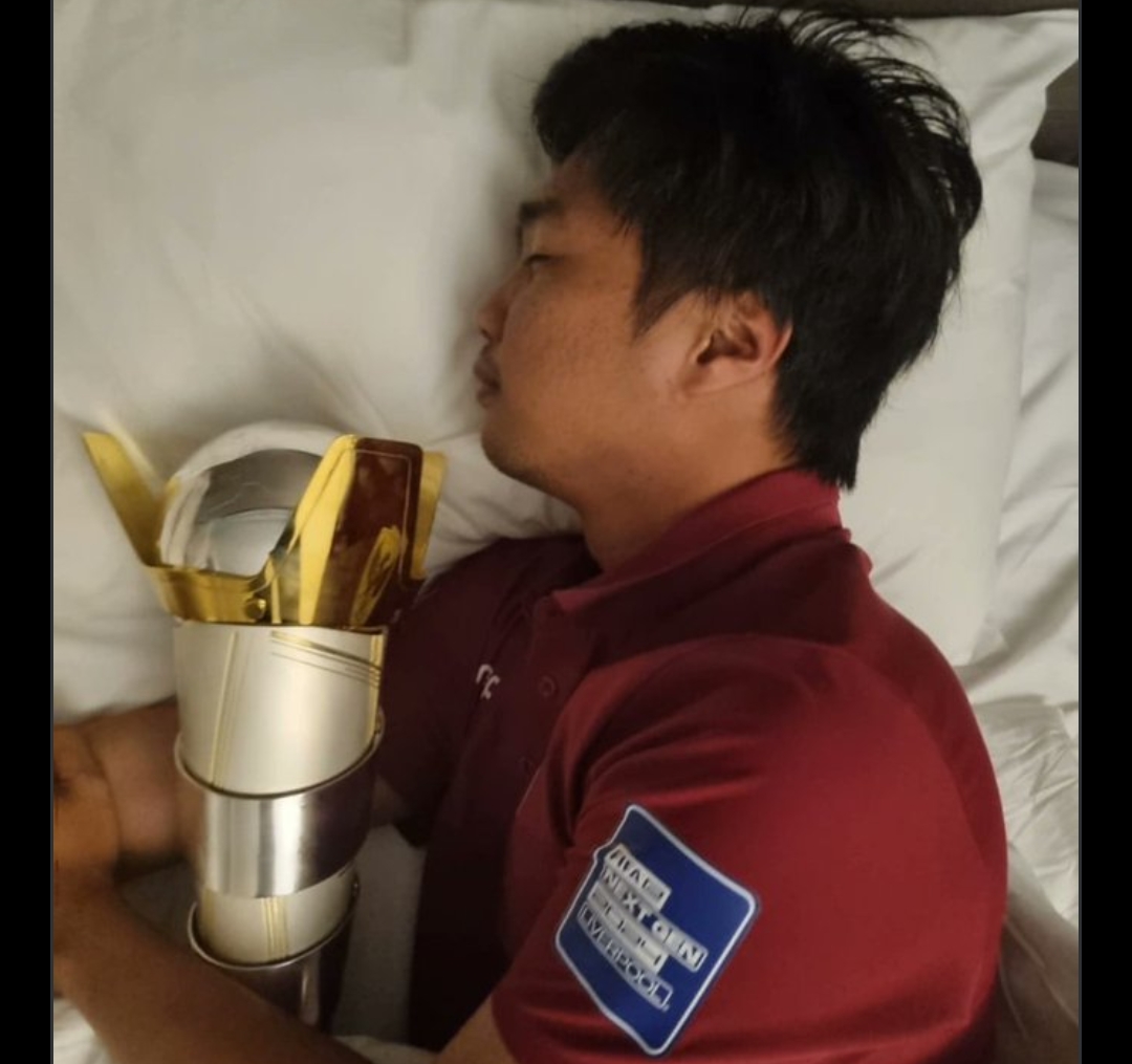 Ichsan Taufiq tidur dengan memeluk trofi juara dunia Football Manager 2024. (X @ichsanopiick) - Image