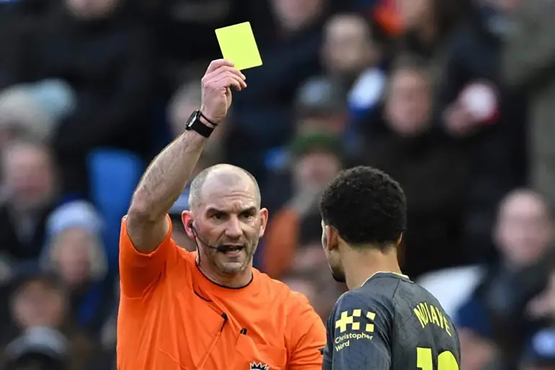 Wasit Tim Robinson (kiri) memberikan kartu kuning kepada pemain Iliman Ndiaye usai mencetak gol. (AFP via Jawa Pos) - Image