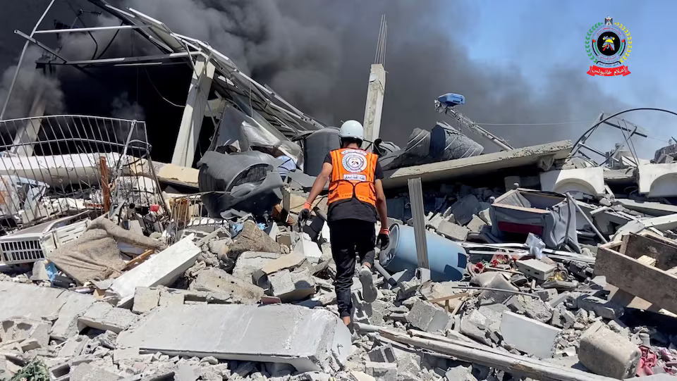 Seorang penyelamat di Gaza yang berjalan di atas puing-puing bangunan untuk menilai kerusakan dan mencari korban selamat. (Reuters/Palestinian Civil Defense) - Image