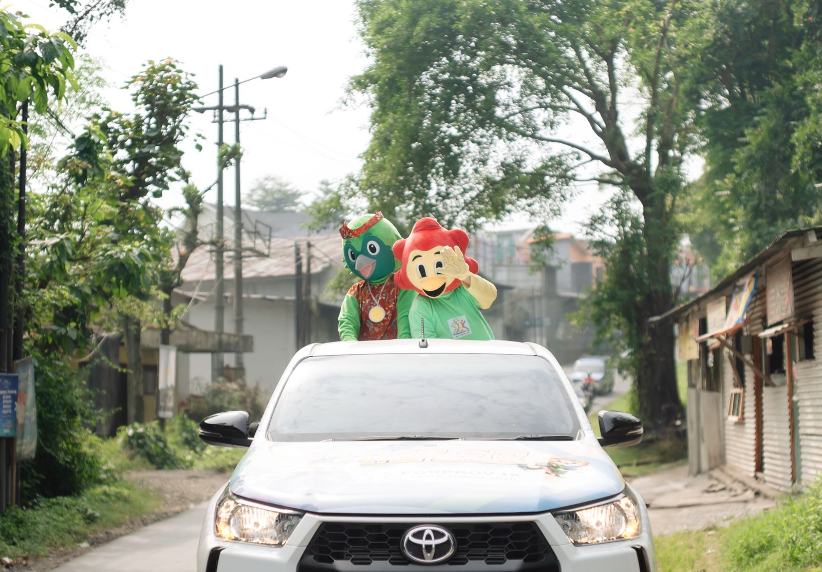 Dua maskot Porprov IX Jatim 2025, Cak Beki dan Cak Jo, menyapa warga dari atas mobil kirab saat melintasi wilayah Kabupaten Malang, Selasa (24/6). (Istimewa) - Image