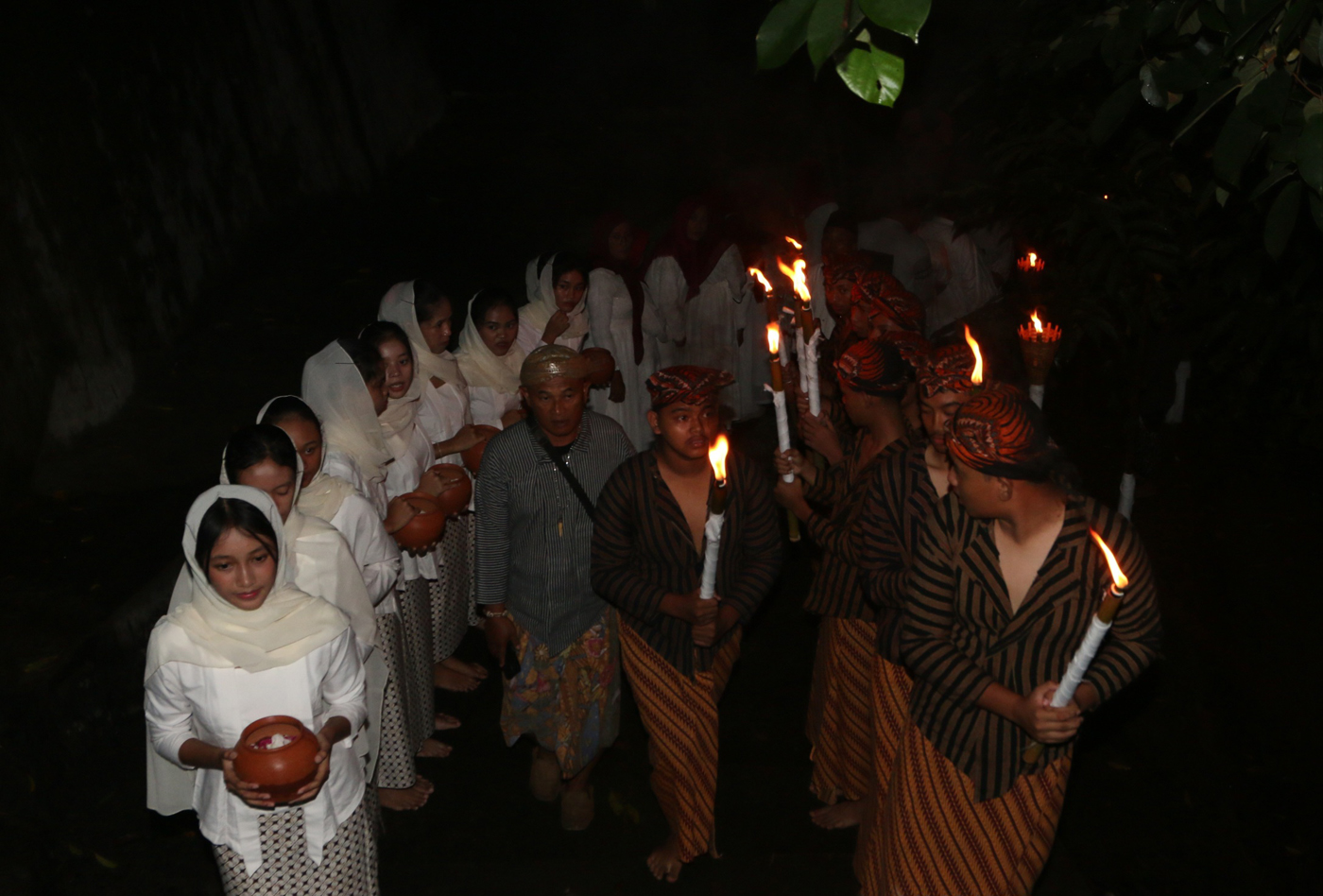 Sejumlah warga mengenakan pakaian tradisional membawa obor dan kendi berisi air dari sendang saat tr