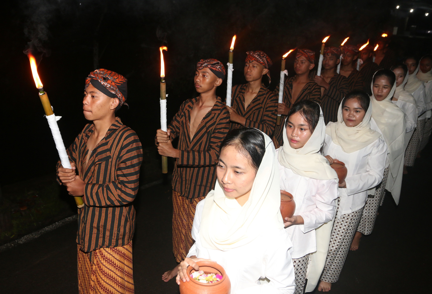 Sejumlah warga mengenakan pakaian tradisional membawa obor dan kendi berisi air dari sendang saat tr