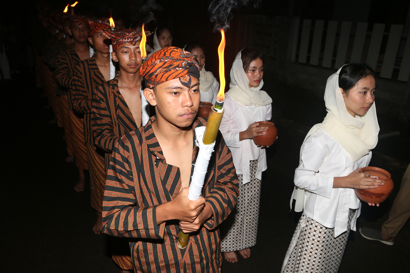 Sejumlah warga mengenakan pakaian tradisional membawa obor dan kendi berisi air dari sendang saat tr