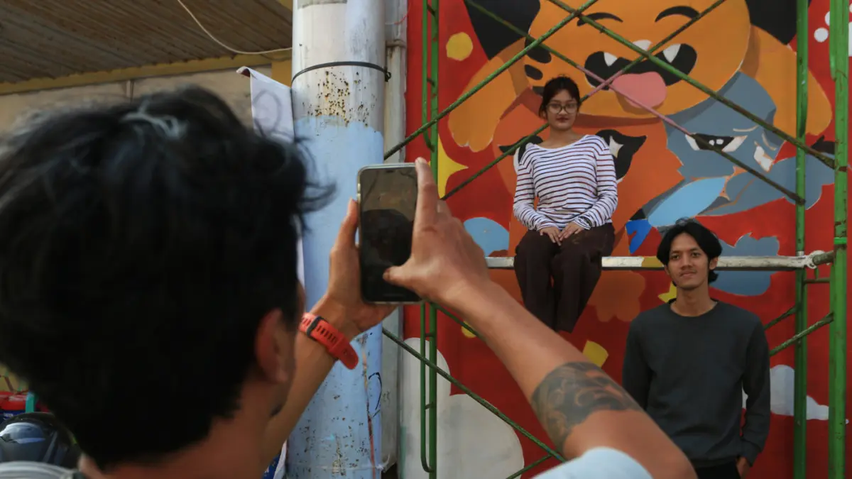 Warga melintas di mural bertema “Aturan Awuren” di tembok Kampung Petemesan, Pekojan, Semarang. (Nur Chamim/ Jawa Pos Radar Semarang)