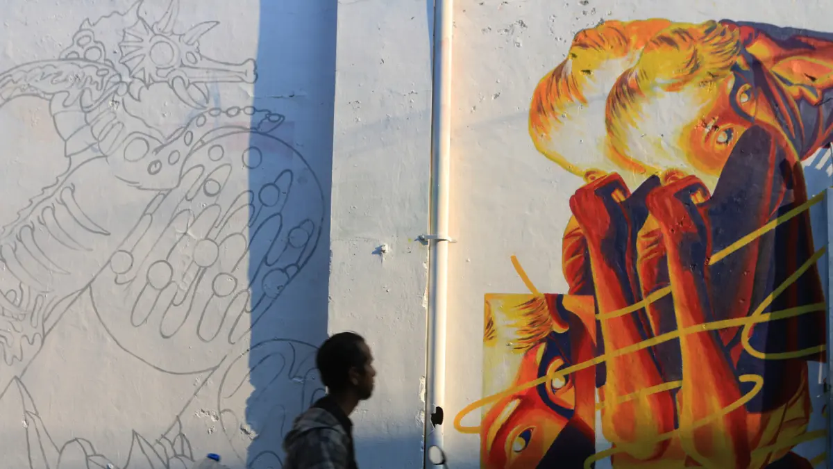 Warga melintas di mural bertema “Aturan Awuren” di tembok Kampung Petemesan, Pekojan, Semarang. (Nur Chamim/ Jawa Pos Radar Semarang)