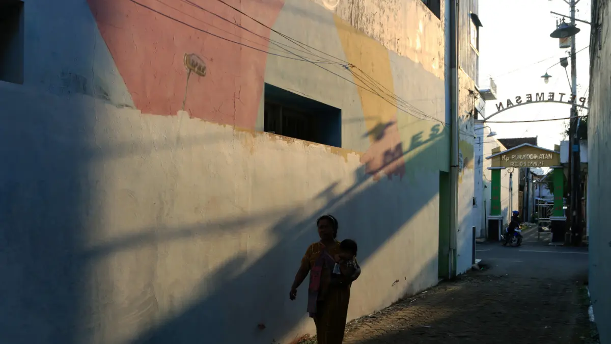 Warga melintas di mural bertema “Aturan Awuren” di tembok Kampung Petemesan, Pekojan, Semarang. (Nur Chamim/ Jawa Pos Radar Semarang)