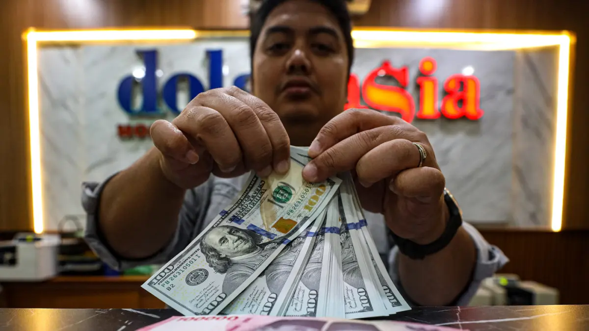 Pegawai menunjukan mata uang dolar AS dan rupiah di salah satu gerai penukaran mata uang asing di Jakarta, Selasa (14/4/2026). (Salman Toyibi/Jawa Pos)