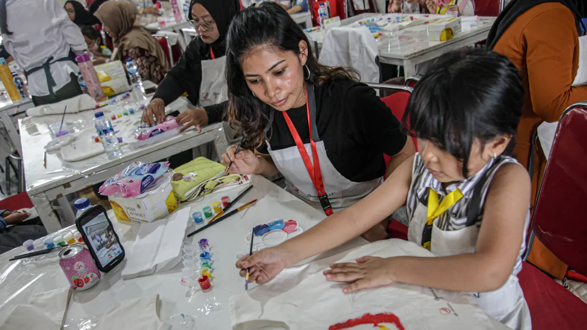 Sejumlah anak-anak didampingi orang tua mewarnai tas kanvas saat kegiatan Re:Art LRT Jakarta Art for Happy Moms and Kids di Stasiun LRT Pulomas, Jakarta, Minggu (19/04/2026). (Hanung Hambara/Jawa Pos)