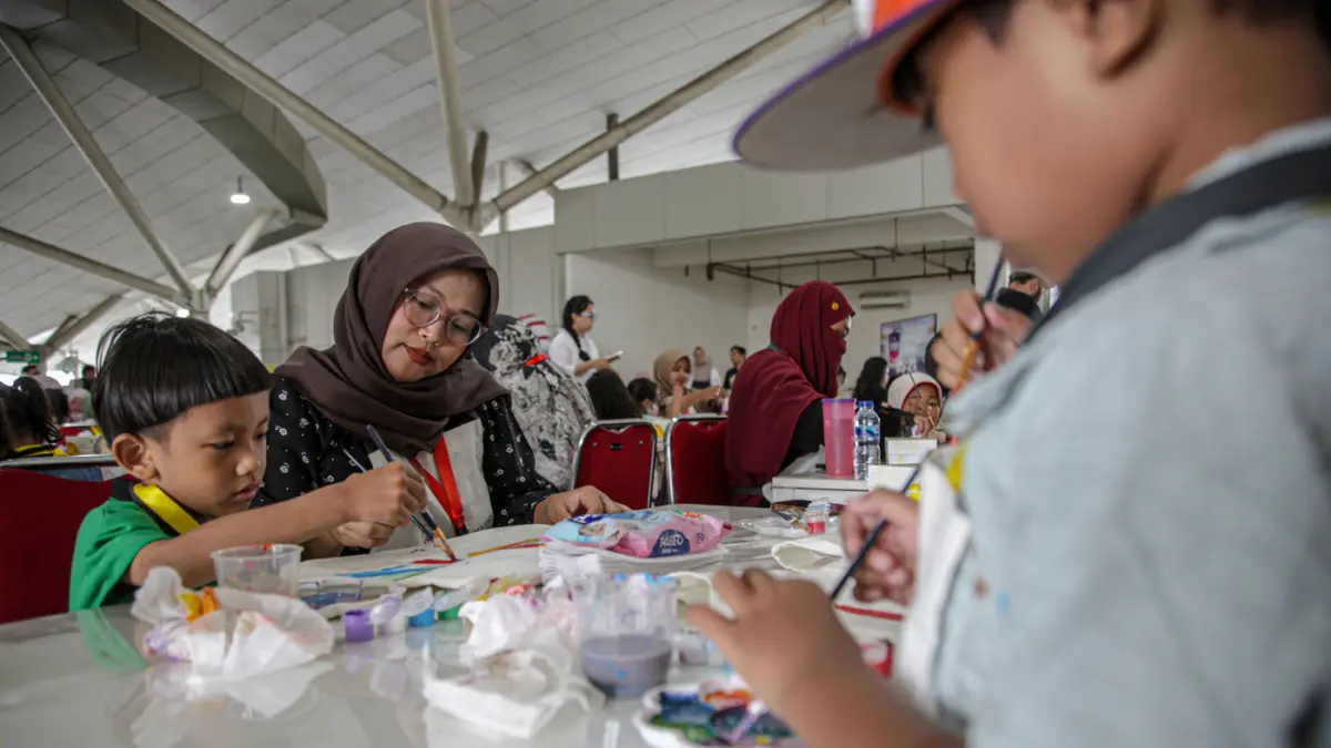 Sejumlah anak-anak didampingi orang tua mewarnai tas kanvas saat kegiatan Re:Art LRT Jakarta Art for Happy Moms and Kids di Stasiun LRT Pulomas, Jakarta, Minggu (19/04/2026). (Hanung Hambara/Jawa Pos)