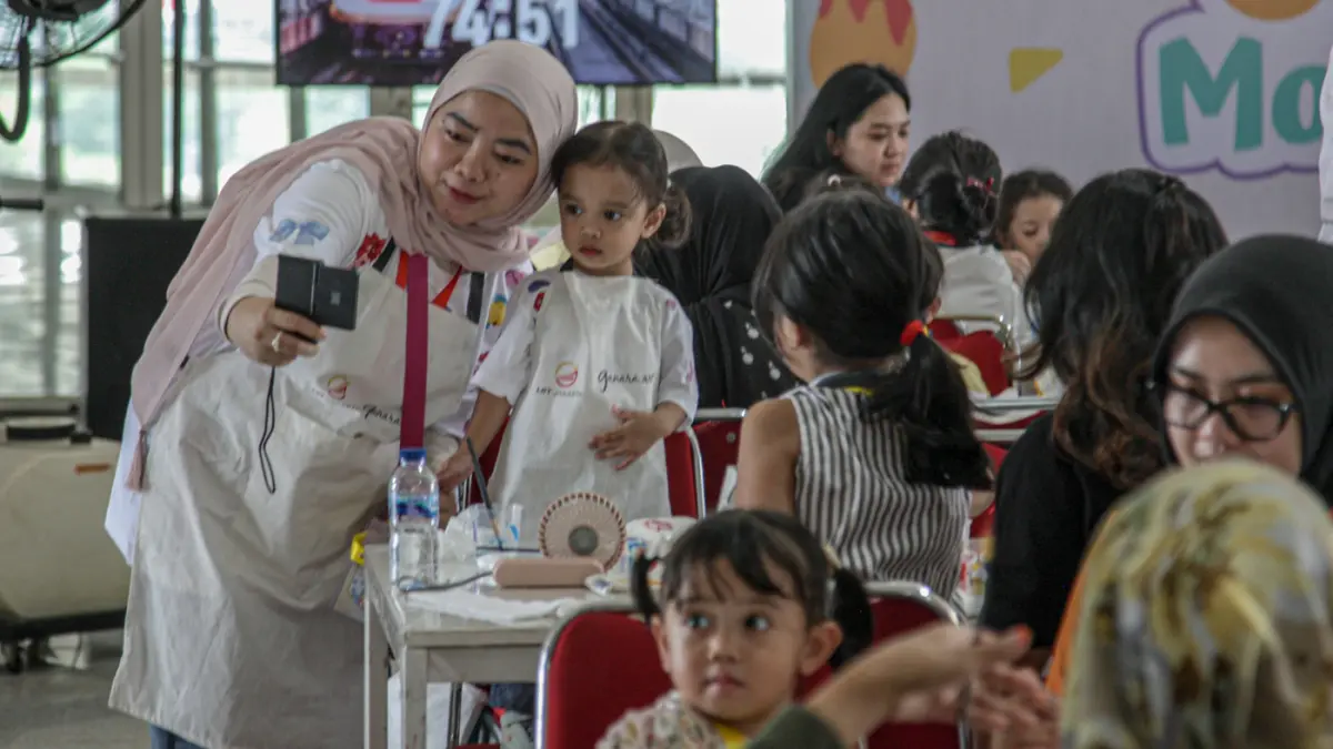 Sejumlah anak-anak didampingi orang tua mewarnai tas kanvas saat kegiatan Re:Art LRT Jakarta Art for Happy Moms and Kids di Stasiun LRT Pulomas, Jakarta, Minggu (19/04/2026). (Hanung Hambara/Jawa Pos)