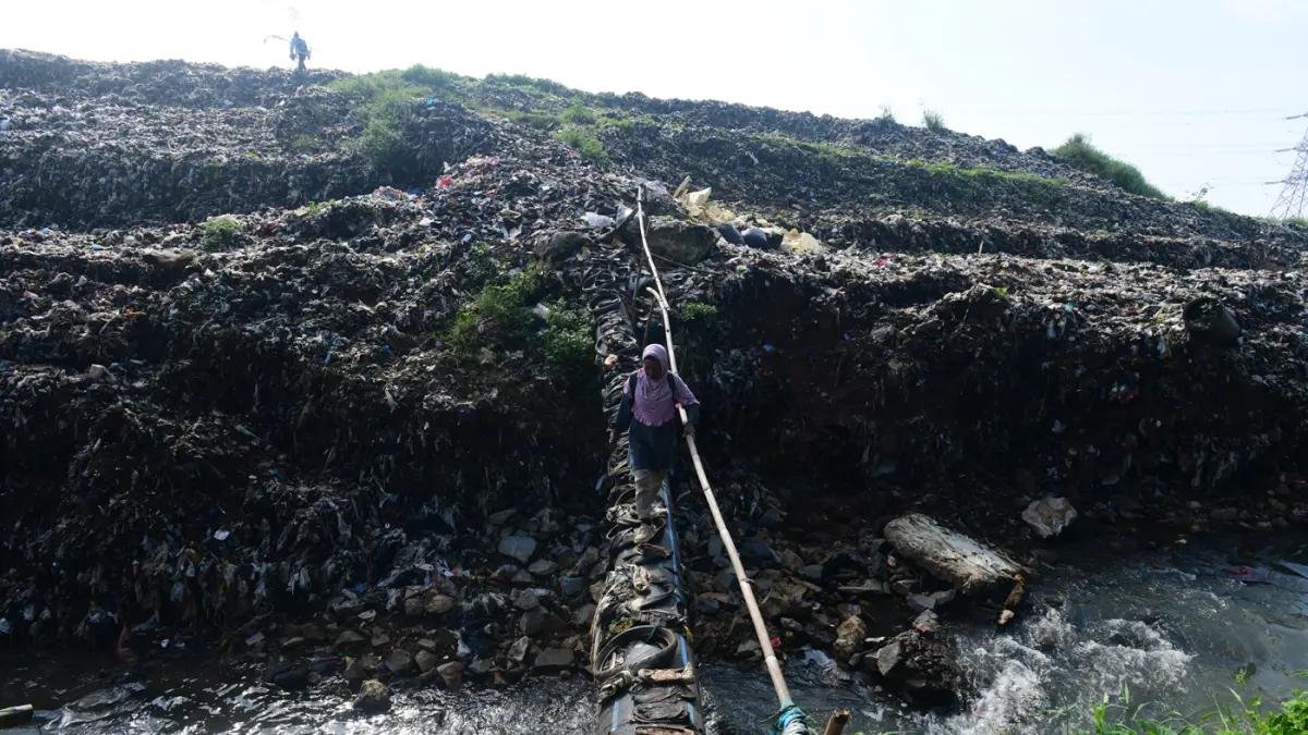 Warga menyebrangi Kali Pesanggrahan yang menyempit akbat longsoran timbunan sampah TPA Cipayung di kawasan Pasir Putih, Depok, Jawa Barat, Senin (27/04/2026). (Dery Ridwansah/ JawaPos.com)