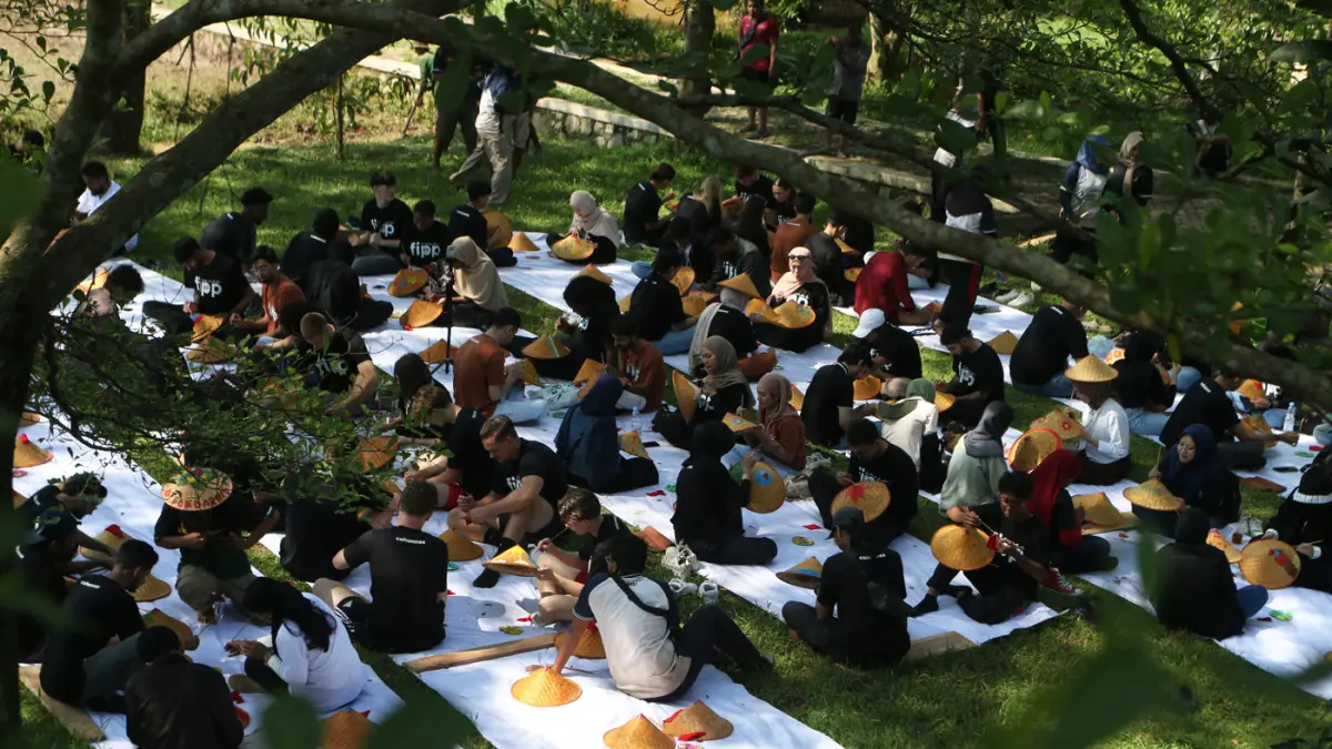 Sejumlah mahasiswa asing melukis caping pada Summer Course UNNES 2026 di desa wisata Kandri, Kota Semarang. (Nur Chamim/Jawa Pos Radar Semarang)