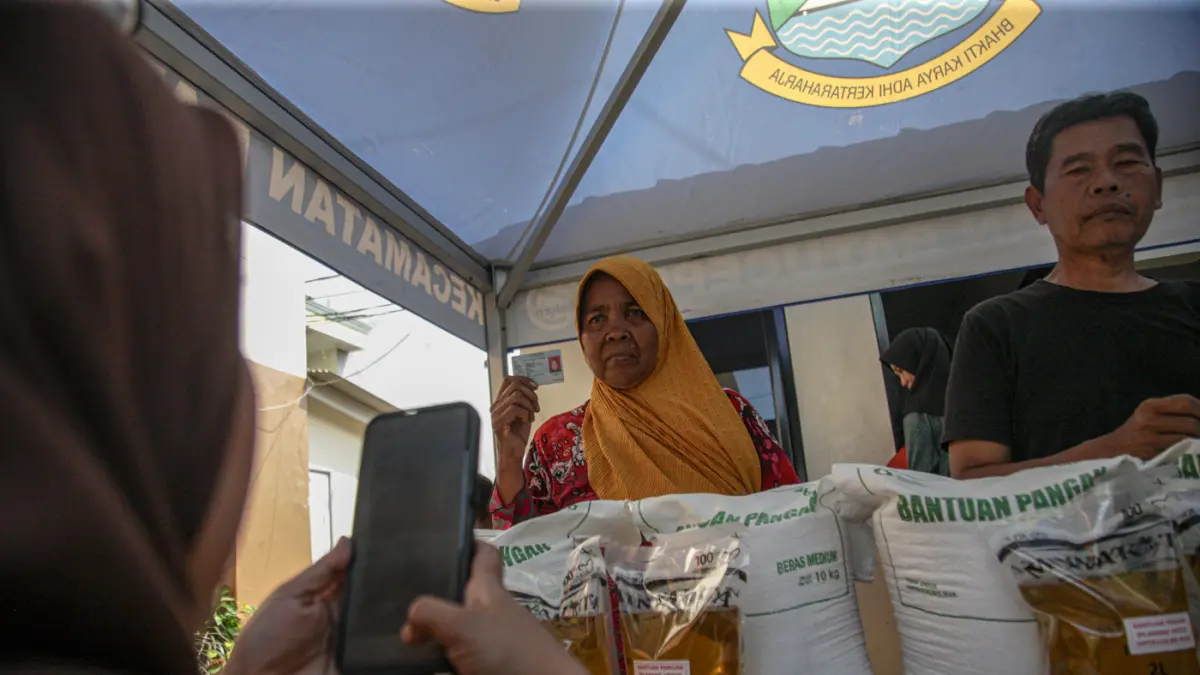 Warga penerima bantuan pangan membawa sejumlah bantuan berupa beras dan minyak goreng saat penyaluran bantuan Keluarga Penerima Manfaat (KPM) di Kantor Kelurahan Batusari, Kota Tangerang, Kamis (14/5/2026). (Hanung Hambara/Jawa Pos)