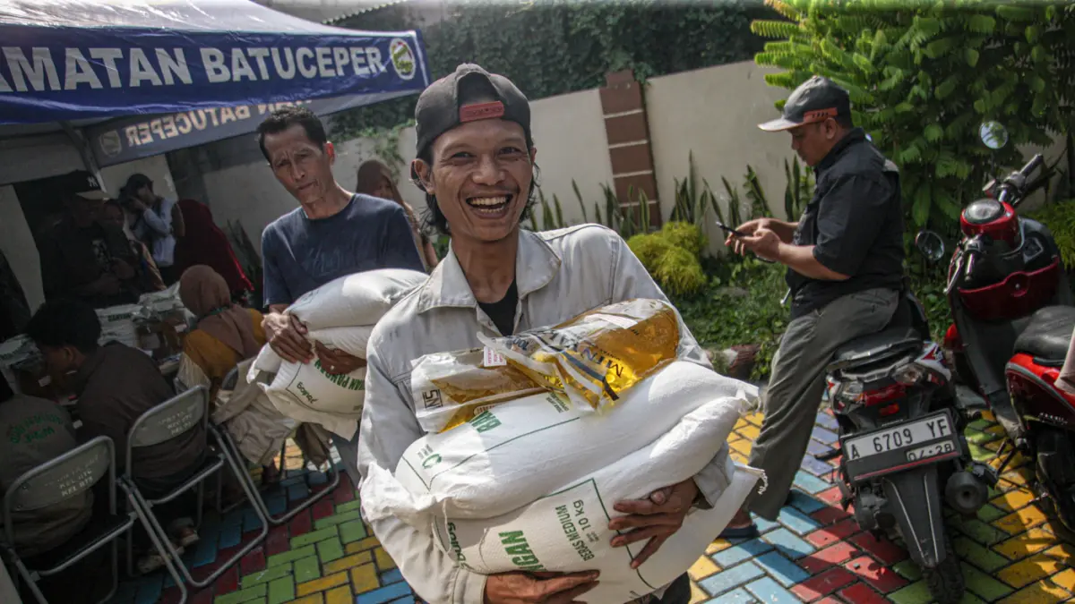 Warga penerima bantuan pangan membawa sejumlah bantuan berupa beras dan minyak goreng saat penyaluran bantuan Keluarga Penerima Manfaat (KPM) di Kantor Kelurahan Batusari, Kota Tangerang, Kamis (14/5/2026). (Hanung Hambara/Jawa Pos)