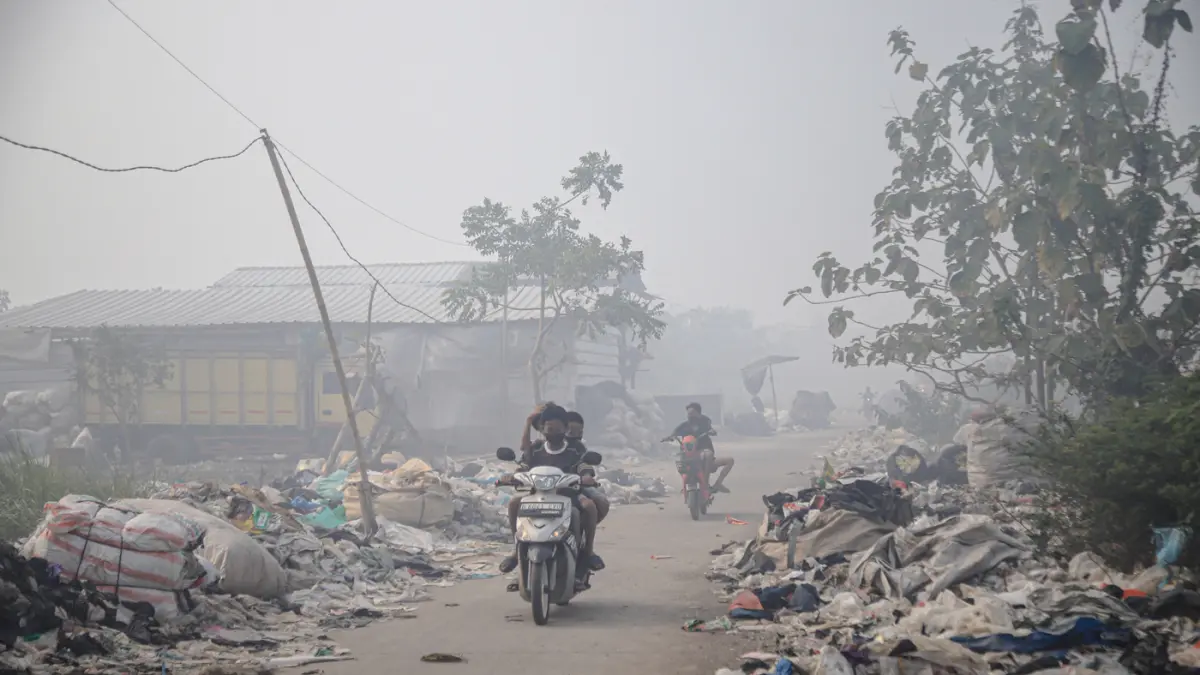 Sejumlah warga beraktifitas ditengah asap kebakaran TPa Jatiwaringin di Desa Tanjakan Mekar, Rajeg, Tangerang, Jumat (03/07/3026). (Hanung Hambara/Jawa Pos)