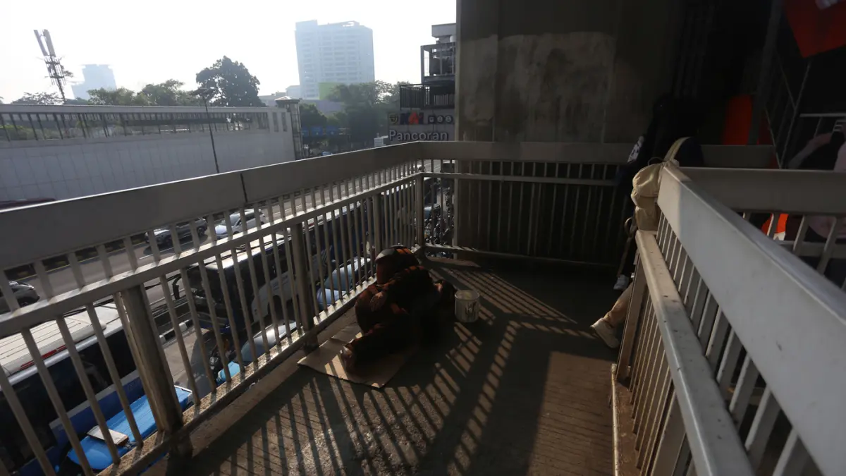 Sejumlah pekerja melintas dekat badut yang tertidur di Kawasan JPO Pancoran, Jakarta Selatan, Senin (20/7/2026). (Dery Ridwansah/ JawaPos.com)