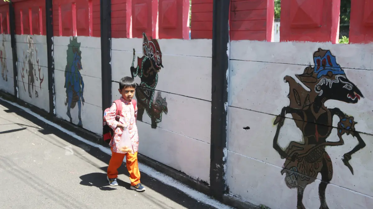 Siswa melintas di tembok pembatas rel latar merah putih dengan lukisan berbagai tokoh wayang,Kota Semarang,Kamis(6/8/2026)