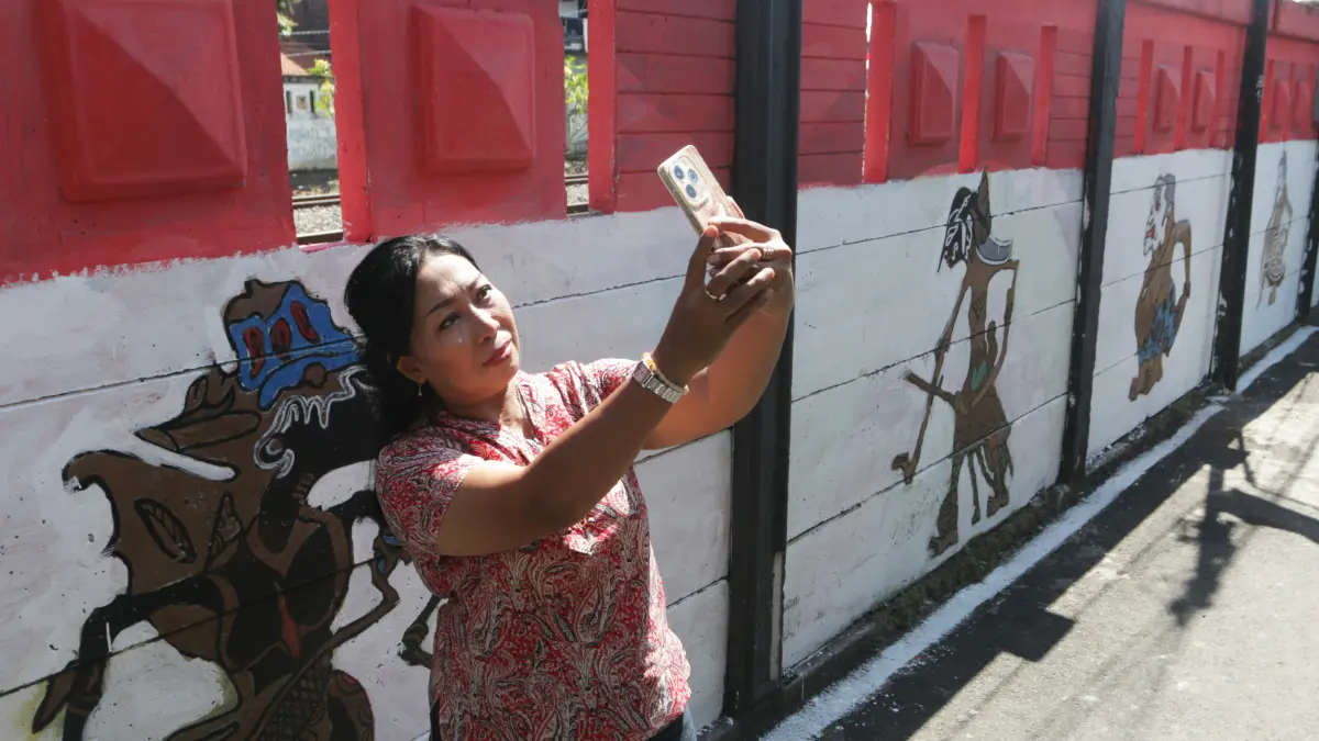 Warga berswafoto di tembok pembatas rel latar merah putih dengan lukisan berbagai tokoh wayang,Kota Semarang,Kamis(6/8/2026)