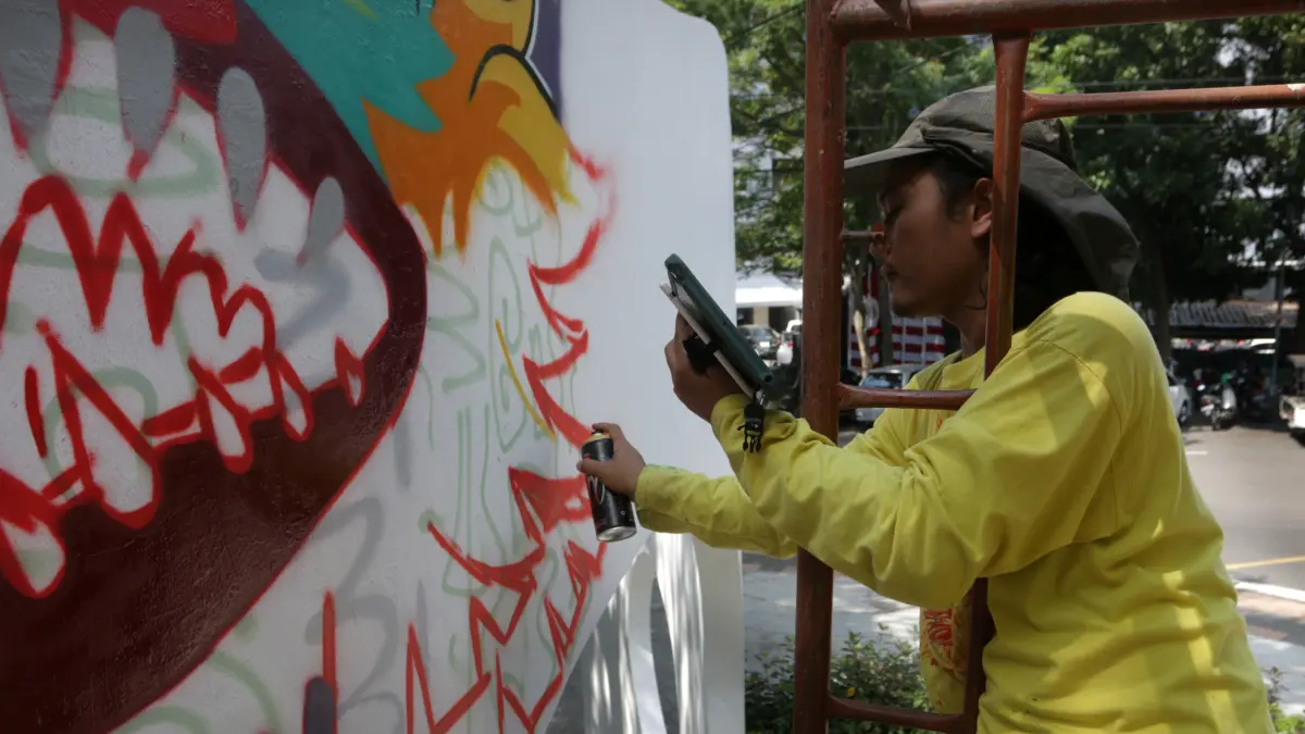 Akari Kokoh Ardanu mengerjakan detail mural dengan cat semprot pada gapura Taman Indonesia Kaya,Kota Semarang, Jumat (7/8/2026)