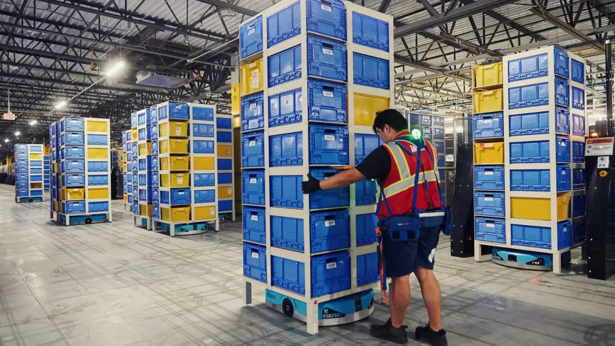 Robot bergerak beroda mengangkut rak-rak tinggi berisi barang di dalam pusat distribusi Amazon (Times of India) - Image