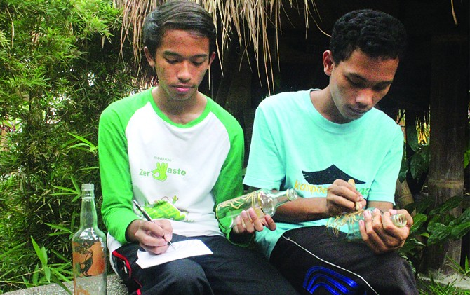 TERUS ASAH KEMAMPUAN: Fajar dan John berkonsentrasi membuat ukiran grafir kaca di botol bekas sirup di Kampoeng Sinaoe pada Sabtu (25/2). - Image