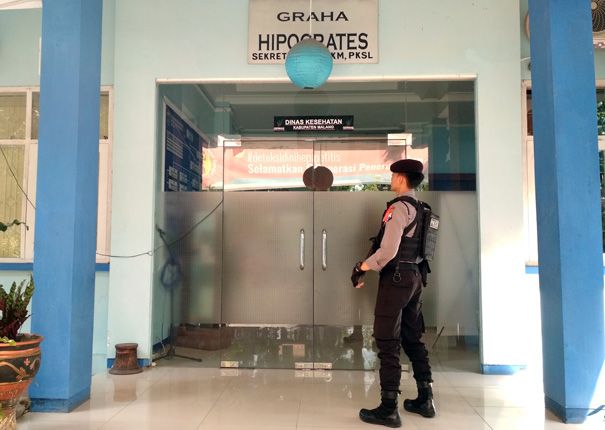 PENGAMANAN KETAT: Personel kepolisian berjaga di depan pintu masuk Dinas Kesehatan. Setidaknya, enam personel KPK tengah melakukan penggeledahan di dinas ini. - Image