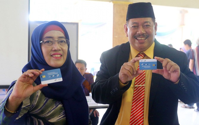 Pasangan suami istri H Adi Suwardoyo dan Hj Siti Choiriyah menunjukkan kartu E Votting sebelum menuju bilik suara. - Image