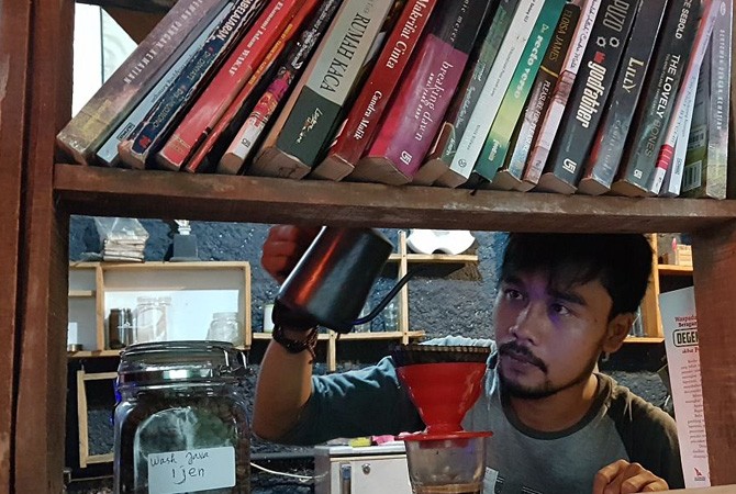 Barista sekaligus Pemilik Kedai Kopi Saung Perjuangan sedang menyeduh kopi sambil menawarkan buku-buku bacaan di kedainya, Minggu (10/3). - Image