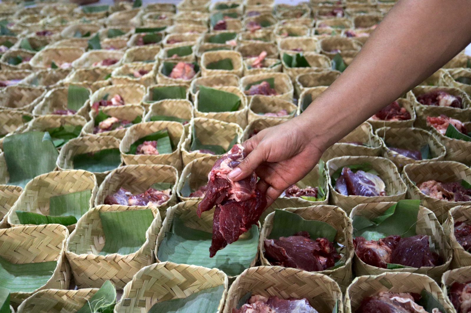 Petugas kurban mengemas daging kurban menggunakan besek yang terbuat dari anyaman bambu di Kebayoran Lama, Jakarta, Minggu (11/8/2019). Penggunaan wadah daging kurban yang terbuat dari bambu ini dilakukan sebagai pengganti plastik. Hal ini dilakukan untu - Image