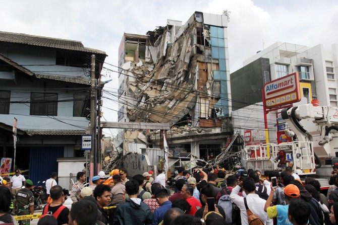 Petugas berjaga -jaga di sekitaran gedung ambruk di Jalan Brigjen Katamso, Kota Bambu Selatan, Palmerah, Jakarta Barat, Senin (6/1/2020). Terlihat bangunan itu menimpa minimarket Alfamart yang berada di lantai dasar. Foto: Dery Ridwansah/ JawaPos.com - Image