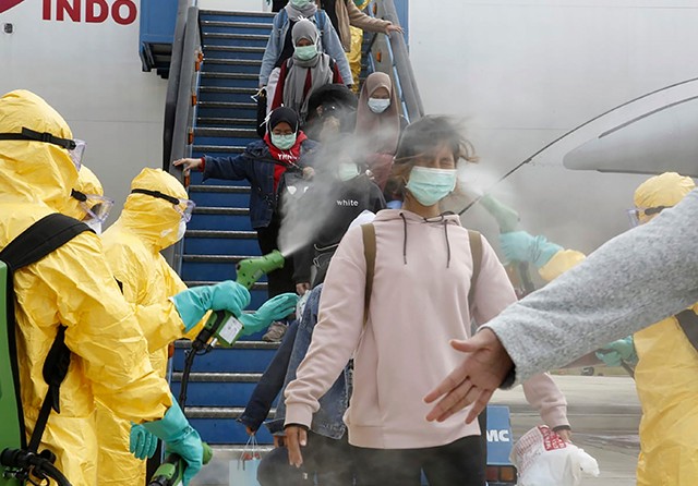 MENUJU KARANTINA: WNI yang dievakuasi dari Wuhan disemprot cairan disinfektan saat turun dari pesawat di Bandara Hang Nadim, Batam, Minggu (2/2). (Indonesian Foreign Ministry via AP) - Image