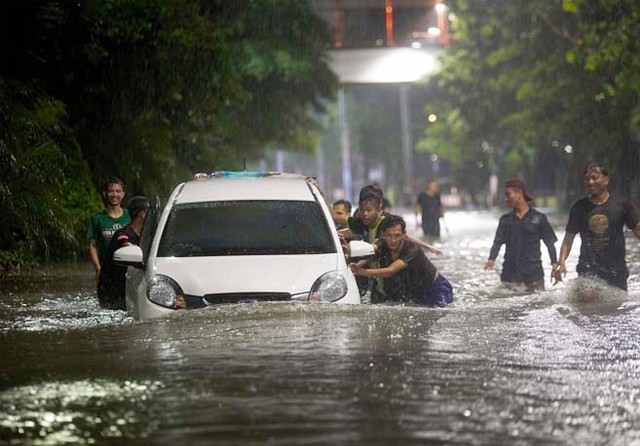 BANTU PENGENDARA: Warga mendorong mobil yang mogok di Jalan Mayjen Sungkono. Ketinggian air mencapai 80 cm. (Riana Setiawan/Jawa Pos) - Image