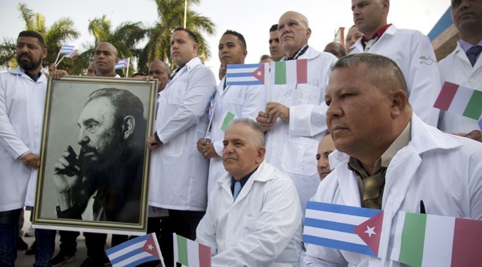 Several of the Cuban doctors and medical professionals that will depart for Italy to assist with the pandemic in the country pose for the media with a photo of Fidel Castro and flags of Italy and Cuba, in Havana, Cuba, Saturday, March 21, 2020. (AP Photo/ - Image