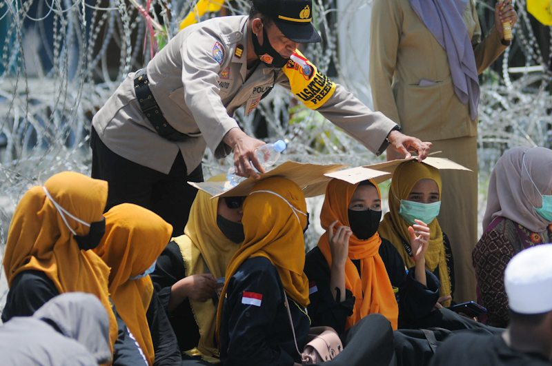Salah seorang aparat kepolisian Polda Sulteng membantu mahasiswa wanita memegang kardus dari terik matahari dalam aksi demo penolakan Omnibus Law di Jalan Samratulangi, Palu, Sulteng, Selasa (13/10). Penolakan terhadap Omnibus Law terus mengalir dari seju - Image