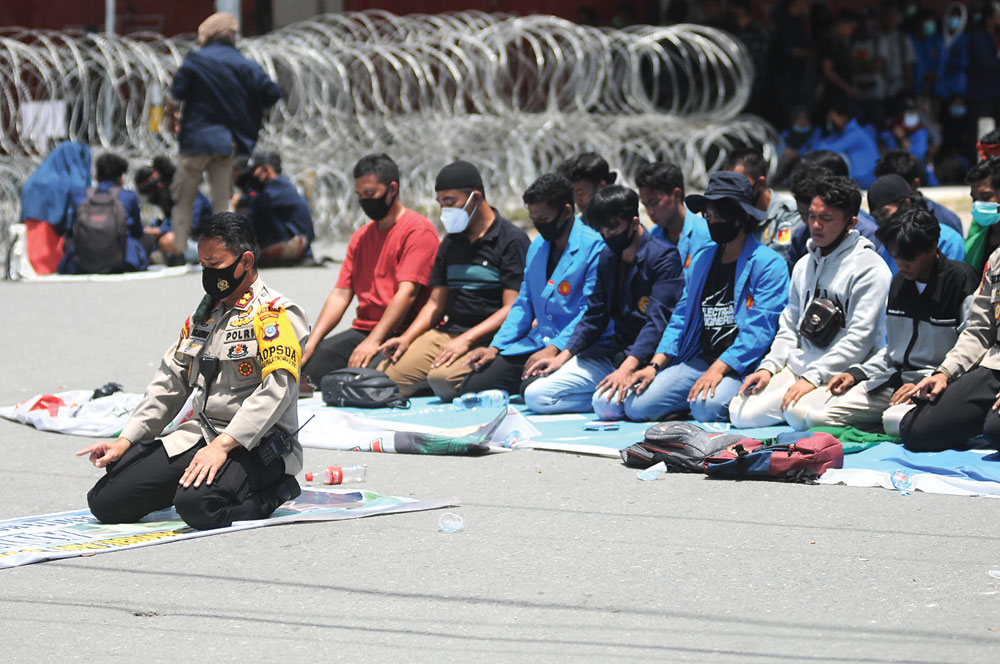 DI SELA-SELA DEMONSTRASI: Aparat kepolisian yang menjaga aksi demonstrasi menolak omnibus law oleh mahasiswa se-Kota Palu, Sulawesi Tengah, menggelar salat berjamaah di jalan kemarin (12/10) bersama sejumlah mahasiswa. Pada aksi pertama 8 Oktober lalu dem - Image