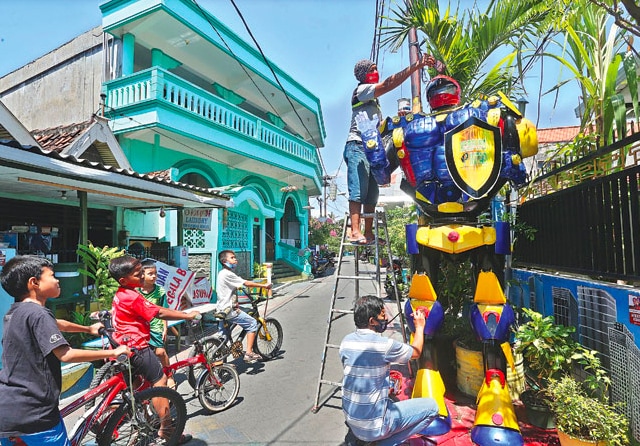 Warga Tembok Gede III mengecat robot Kampung Pintar yang terbuat dari limbah PJU dan TV. (Ahmad Khusaini/Jawa Pos) - Image